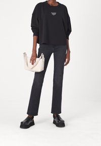 Felpa nera in cotone con vestibilità oversize e logo. Jeans in denim scuro a vita alta e zoccoli neri con plateau. Borsa a tracolla bianca con tracolla con logo.