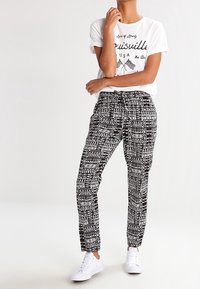 Pantalon à motifs noir et blanc, coupe décontractée avec taille élastique, associé à un t-shirt blanc à motif graphique et des baskets blanches.