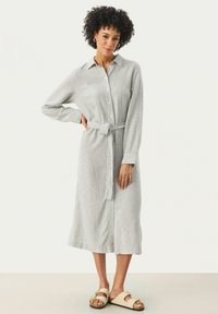 Abito a camicia a righe con maniche lunghe in grigio chiaro e bianco, con chiusura a bottoni, vita legata e vestibilità comoda. Abbinato a sandali neutri.