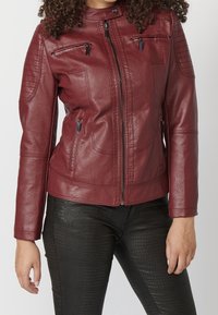 Burgundowa skórzana kurtka o dopasowanym kroju, z zamkiem z przodu i kieszeniami. Posiada pikowane akcenty na ramionach oraz gładką teksturę.