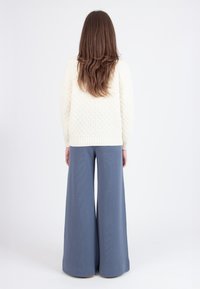 Suéter de color crema, tejido, con un patrón texturizado y un dobladillo acanalado; combinado con pantalones de pierna ancha de color azul claro, hechos de un material suave.