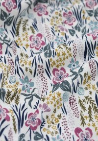 Tessuto di cotone con un motivo floreale che presenta accenti in viola, blu e oro su uno sfondo bianco, con foglie di forme e dimensioni variabili.