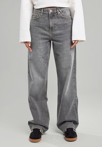 Jeans gris taille haute et large en denim, avec une texture délavée, cinq poches, et une fermeture à bouton en laiton et à zip.