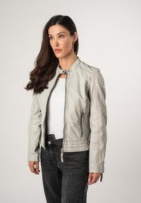 Giacca in pelle grigia chiara con colletto, zip frontale, tasche laterali e dettagli trapuntati all'orlo. Indossata sopra una maglietta bianca e pantaloni neri.