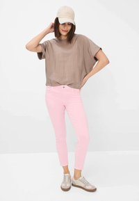 Maglia chiara a maniche lunghe, jeans skinny rosa e sneakers beige. Sfondo bianco, stile casual, design minimalista.