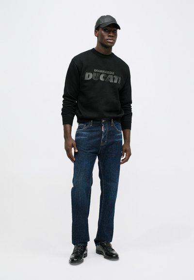 Zwarte sweatshirt met verhoogde tekst "DSQUARED2 DUCATI", blauwe jeans met subtiele textuur en zwarte leren schoenen, allemaal tegen een neutrale achtergrond.
