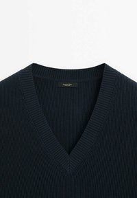 Marinblå ribbad stickad tröja med V-ringning. Har ett strukturerat tyg och en liten etikett vid halsringningen.