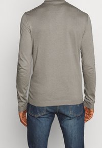 Ljust grå långärmad skjorta med rundad halsringning, tillverkad av mjukt tyg. Matchas med blå denimjeans med subtila sömnadsdetaljer.