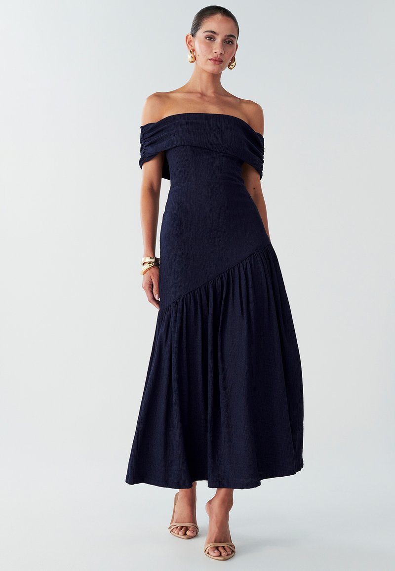 Robe épaules dénudées bleu marine foncé avec tissu texturé. Corsage ajusté, jupe évasée avec détails froncés. Complétée par des talons à brides.