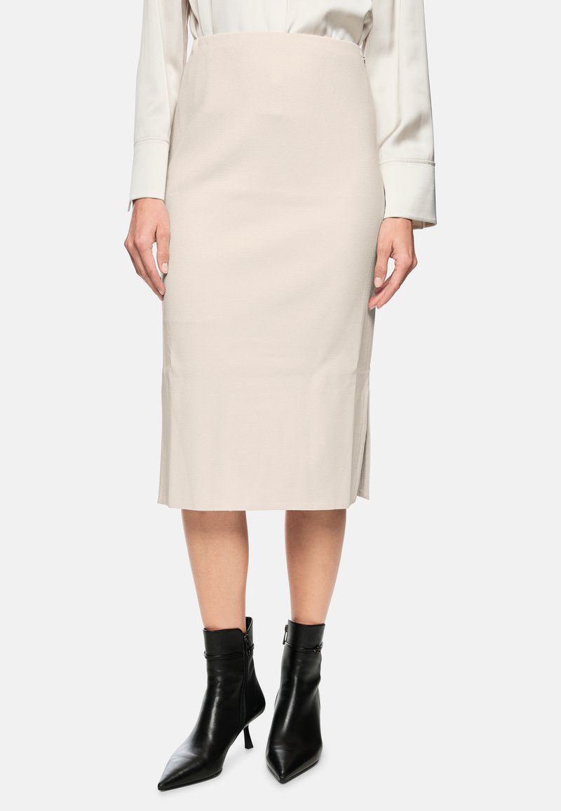 Beige Bleistiftrock mit glatter Textur, schlanker Schnitt und seitlichen Schlitzungen. Kombiniert mit schwarzen spitzen Knöchelstiefeln.