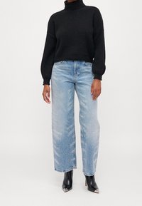 Czarny dziany sweter z golfem, jasne jeansy o prostych nogawkach z błyszczącymi detalami oraz czarne botki z noskami w szpic.