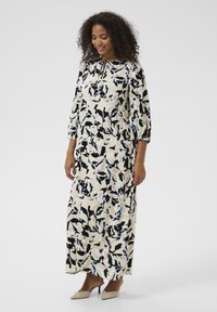 Maxi dress in cream featuring a floral pattern in black and light blue. Long sleeves with a gathered neckline, soft fabric, and relaxed fit.