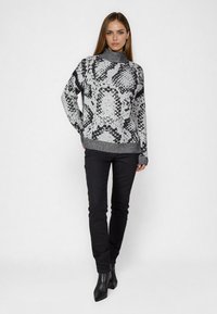 Black and white patterned sweater with a high neckline, long sleeves, and ribbed cuffs, paired with black fitted pants and pointed boots.