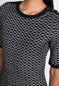 Czarny i biały krótki rękaw top z wzorem fal, z okrągłym dekoltem i guzikami na ramieniu. Teksturowany materiał dziany.