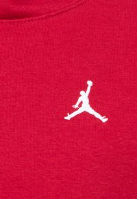 Tissu en coton rouge avec un logo Jumpman blanc. La texture est douce avec un léger élasticité, et l'encolure a un design classique en col rond.
