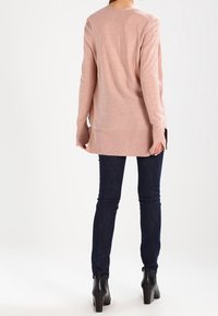 Light pink long-sleeve sweater with a ribbed texture, side slits, and a relaxed fit, paired with dark blue skinny jeans and black ankle boots.