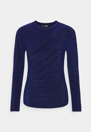 Maglia a maniche lunghe di un blu profondo con una texture scintillante. Presenta un collo rotondo e dettagli drappeggiati sul davanti.