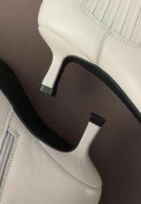 Chaussures à talons hauts en cuir crème avec des accents noirs, présentant des coutures verticales et un design à bout pointu.