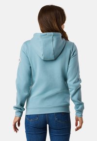 Lichtblauwe hoodie met een eenvoudig ontwerp, voorzien van een capuchon, ribgebreide manchetten en zoom. Soepele textuur en een cirkelvormig logo op de linkermouw.