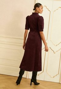 Sametine burgundi kleit lühikeste puhv-sammetega, vöökoht, ja voogav seelik, koos põlvini ulatuvate mustade kontsadega saapatega.