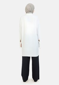 Tunic bianca oversize con maniche lunghe e fessure laterali, abbinata a pantaloni a palazzo a righe blu navy. Il tessuto sembra leggero e liscio.