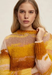 Il maglione a maglia presenta strisce orizzontali in tonalità di giallo, arancione e rosa. Tessuto testurizzato con scollo rotondo e polsini morbidi.