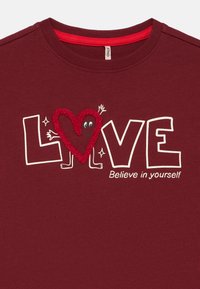 Sweatshirt de manga comprida cor borgonha com a palavra "LOVE" em branco, um coração vermelho texturizado e a frase "Acredite em si mesmo."