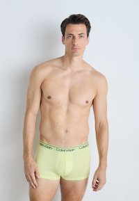 Moške boksarice Calvin Klein v svetlo rumeni barvi, z black logotipom na pasu. Tkanina se zdi gladka in elastična.