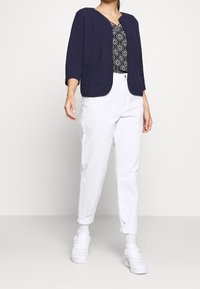 Marinblå blazer med trekvartslånga ärmar, rund halsringning och framfickor. Matchad med vita jeans och vita sneakers. Strukturerad textil.