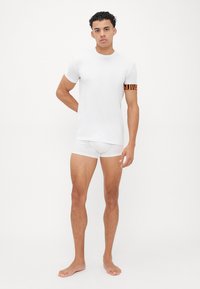 White short-sleeve t-shirt with a striped orange and black accent on the left arm. Worn with white athletic shorts.