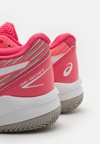 Różowe buty sportowe z fakturowaną cholewką, ozdobione wielokolorowymi paskami na pięcie, białym logo i gumową podeszwą.