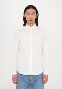 White long-sleeve button-up shirt with a classic collar, made of smooth fabric; paired with light blue denim jeans.