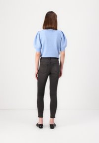 Suéter de punto azul claro de manga corta con mangas abullonadas, combinado con jeans oscuros ajustados y zapatos planos negros.