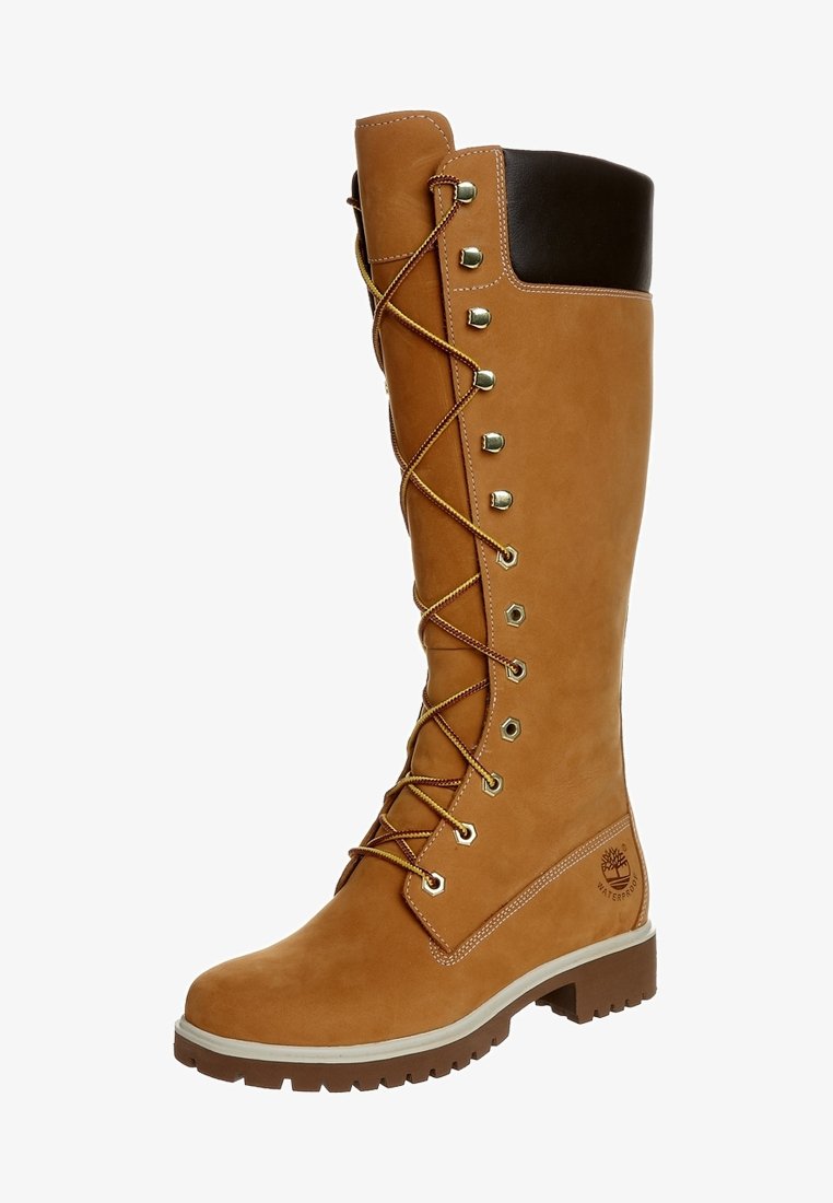 Botte en cuir marron clair montant jusqu'au genou avec des accents bruns, une ferrure dorée et un design à lacets. Elle présente une surface texturée et une semelle en caoutchouc.