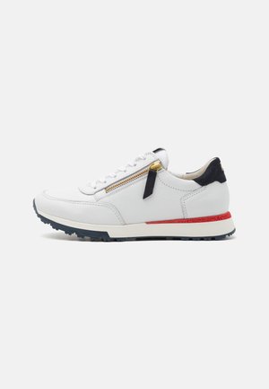 White leather sneaker with black accents, a gold zipper, red stripe on the sole, and a textured finish. Designed for casual wear.