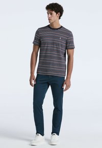 Gestreepte T-shirt in marineblauw en rood met een ronde hals. Gecombineerd met op maat gemaakte donkerblauwe broek en witte sneakers. Gladde stoftextuur.