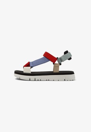 Sandal multicolor con tiras rojas, azules y verdes, una plantilla negra y una suela de goma blanca con surcos texturizados para mejorar la tracción.