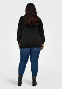 Juodas megztinis su ilgomis rankovėmis ir taškelių detalėmis ant rankovių, derinamas su mėlynomis džinsinėmis kelnėmis ir juodais auliniais batais.