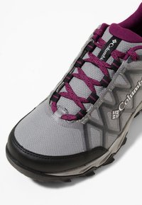 Chaussure de randonnée Columbia grise et noire avec des lacets violets et des étiquettes de marque, avec une semelle texturée et un col de cheville rembourré.