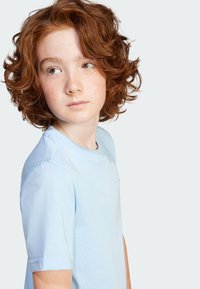 Hellblaues Baumwoll-T-Shirt mit kurzen Ärmeln, Rundhalsausschnitt und subtilen Nahtdetails, getragen von einem Kind mit lockigem roten Haar.