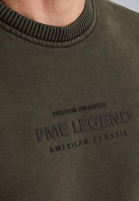 Olive zelená mikina s rebrovaným výstrihom. S výčnelkovým čiernym nápisom: "PME LEGEND" a "FREEDOM UNLIMITED AMERICAN CLASSIC."