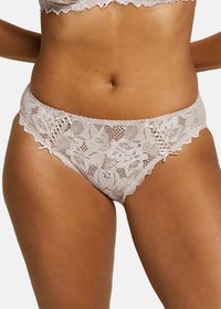 Lingerie en dentelle de couleur beige clair ornée de motifs floraux, de bords scallopés et de détails en ruban sur les côtés. Texture douce et délicate.