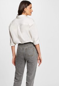 Camicia bianca con colletto, maniche arrotolate, tessuto morbido. Abbinata a jeans grigi a vita alta, con tasche posteriori e dettagli di cucitura sottili.