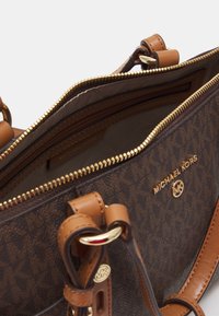 Borsa a tracolla marrone a motivo con chiusura lampo dorata, dettagli in pelle beige e un logo. L'interno presenta una fodera liscia e una tasca con zip.