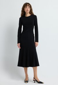 Schwarzes Midi-Kleid mit langen Ärmeln, gerafftem Oberteil und schwingendem Saum. Glatter Stoff mit figurbetonendem Schnitt und minimalen Akzenten.