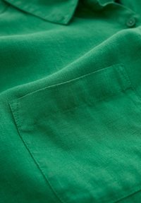 Groene linnen shirt met een kraag en een opgestikte zak. De stof heeft een gestructureerde afwerking met een lichte glans.