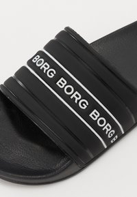 Fekete csúszó szandál széles, texturált pánttal, melyen ismétlődő fehér "BORG" felirat található. Puha talpbetét a kényelem érdekében; lapos talp.
