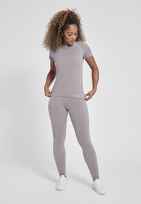 Grå træningssæt med en tætsiddende kortærmet top og leggings med kontrasterende teksturerede paneler og logo-detalje på taljebåndet.