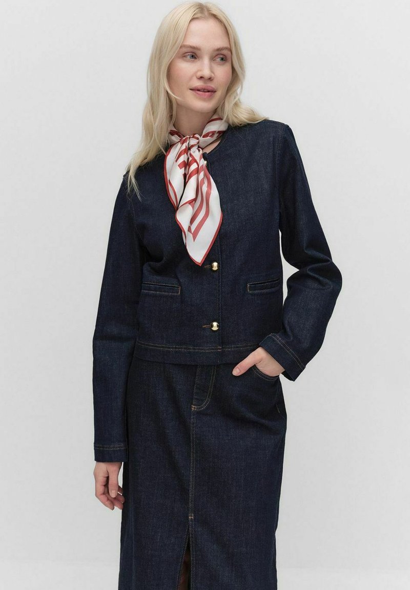 Veste en denim noir à coupe courte, avec des boutons dorés, deux poches avant et une jupe en denim assortie. Une écharpe rayée rouge et blanche est nouée au cou.