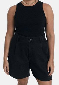 Top de tirantes negro acanalado combinado con pantalones cortos de mezclilla negros de cintura alta que cuentan con bolsillos laterales y un cierre de botón frontal.